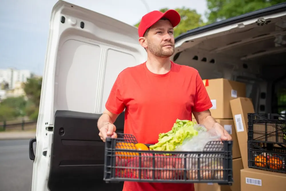Livreur portant une caisse de légumes devant sa camionnette