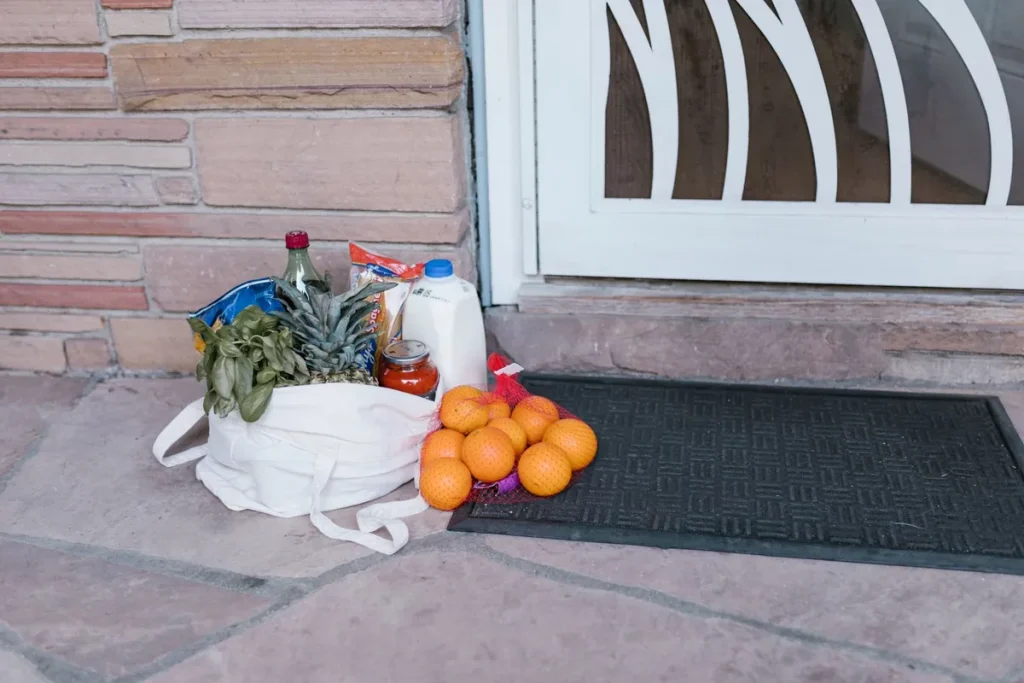 Sac de courses posé sur le pas d'une porte avec légumes, oranges et lait, livré à domicile