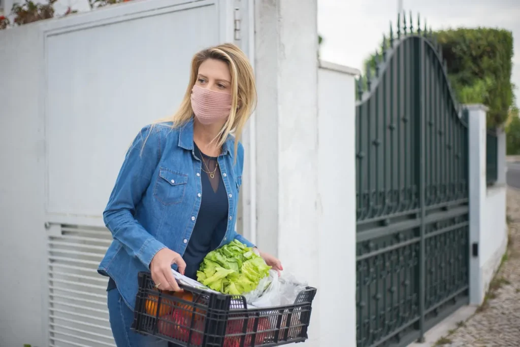 Une femme porte une caisse de salades et de légumes sur le pas d'un portail