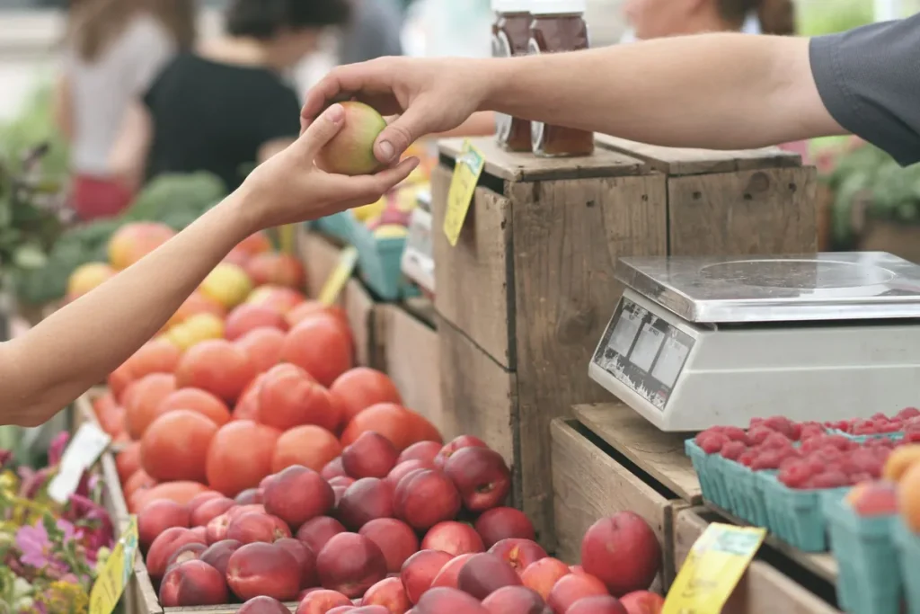 Un client et un commerçant d'étal échangent une pomme devant des fruits et une balance, symbole d'un accord direct avec le producteur