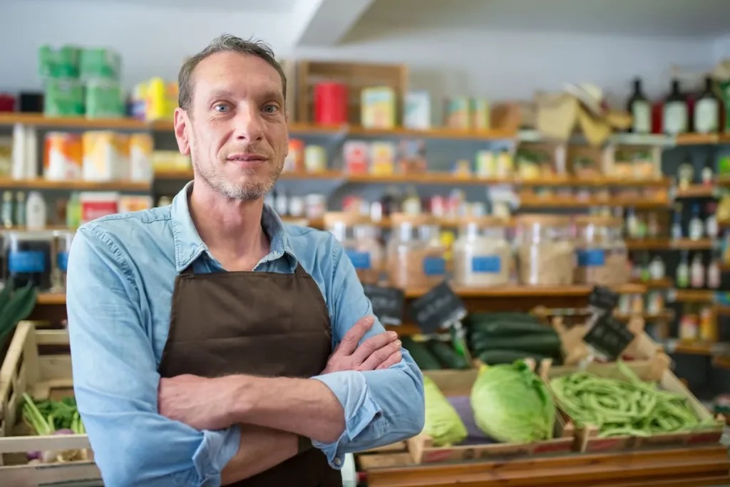 Portrait d'un commerçant en tablier devant ses caisses de légumes frais