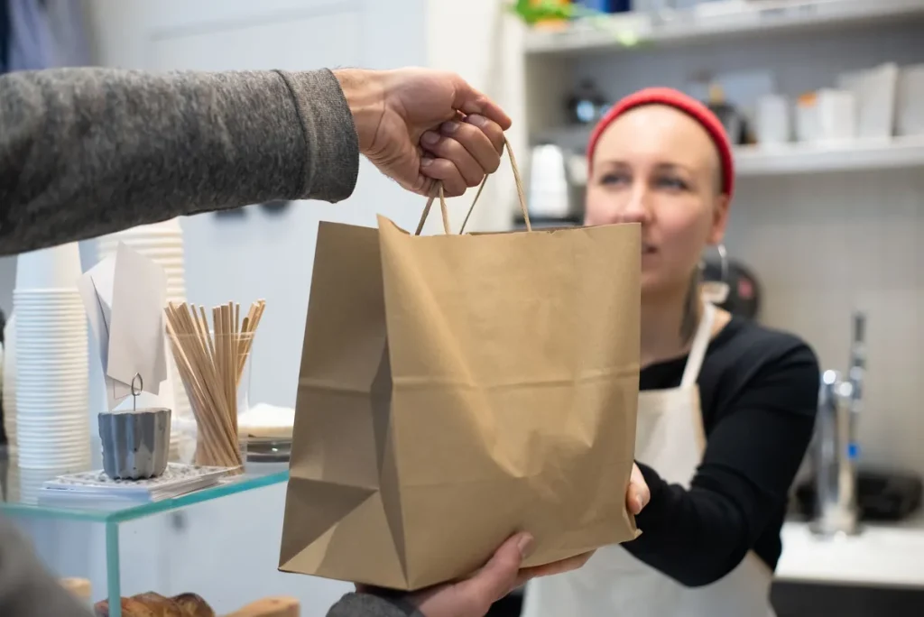 Une commerçante tend un sac en papier kraft à un client au comptoir de retrait